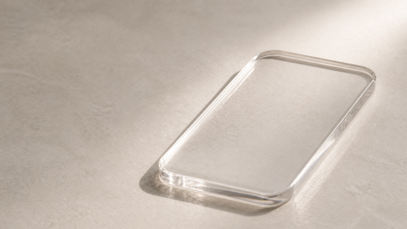 Transparentes, smartphoneförmiges Acrylglasobjekt auf einer hellen Steinoberfläche.